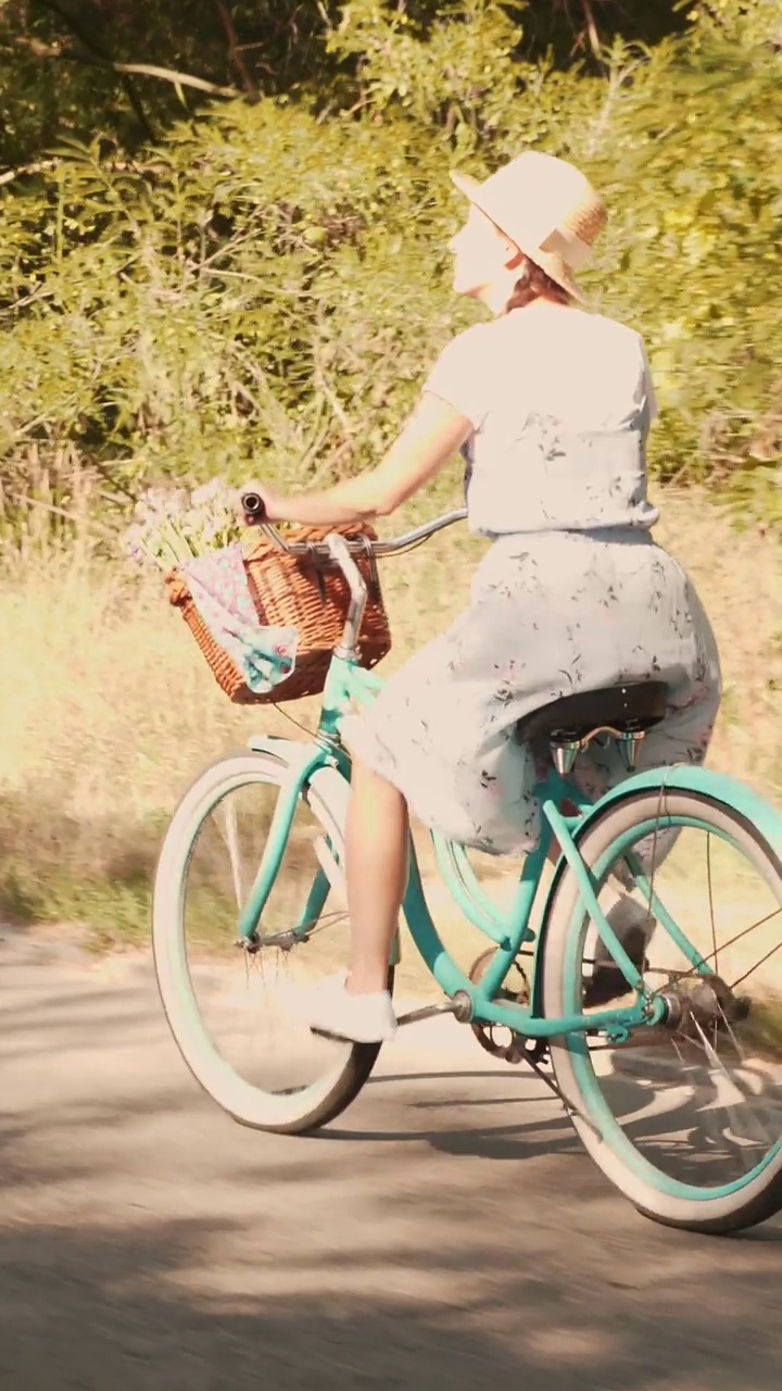 戴草帽穿裙子的女孩在公园里骑着复古的老式自行车。垂直视频视频下载