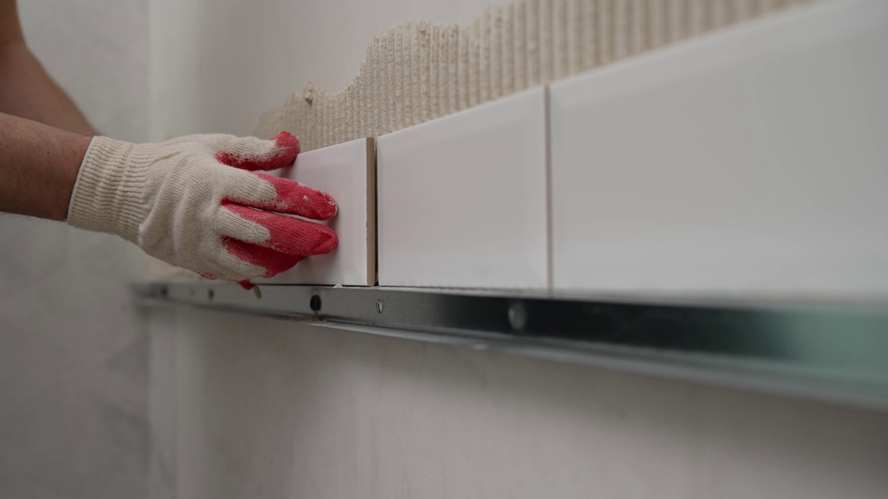 把瓷砖粘在厨房的墙上。勤杂工的手用抹刀在贴好的瓷砖旁边的墙上涂抹瓷砖胶。施工细节、维修工作。视频素材