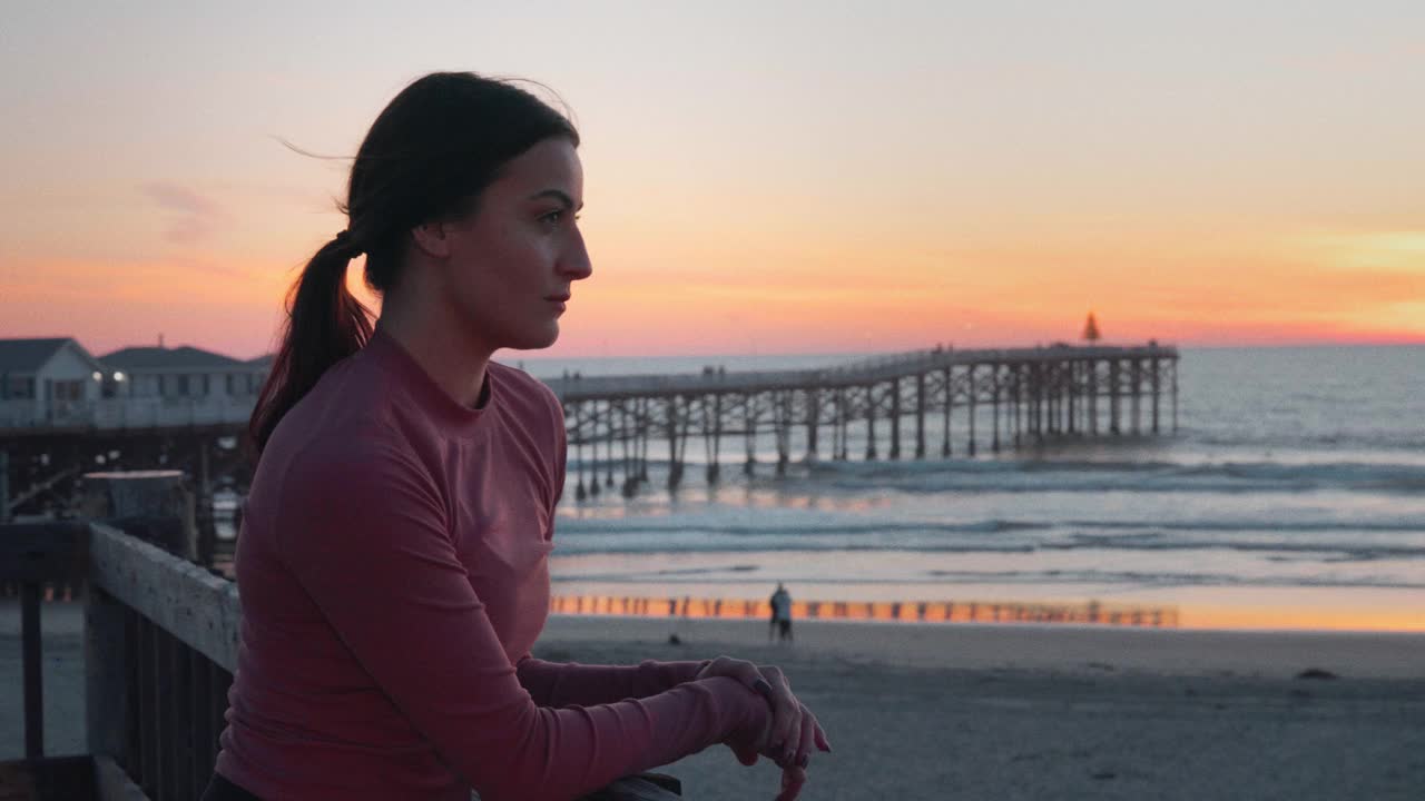 沉思的年轻健康慢跑女子在太平洋海滩水晶码头看日落，圣地亚哥，加利福尼亚视频下载