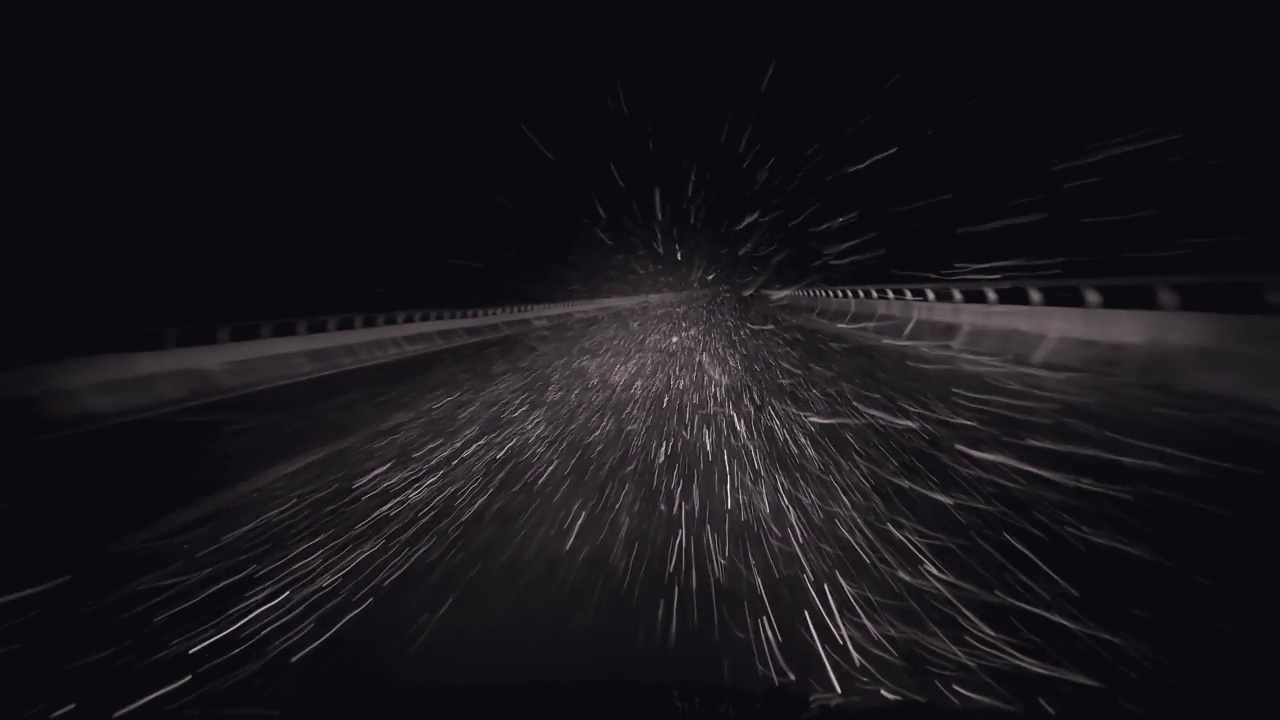 夜晚驾车的pov在湿漉漉的雪滑的高速公路上，雪花打在挡风玻璃上，被车灯的低光束照亮。恶劣天气道路安全运输视频素材