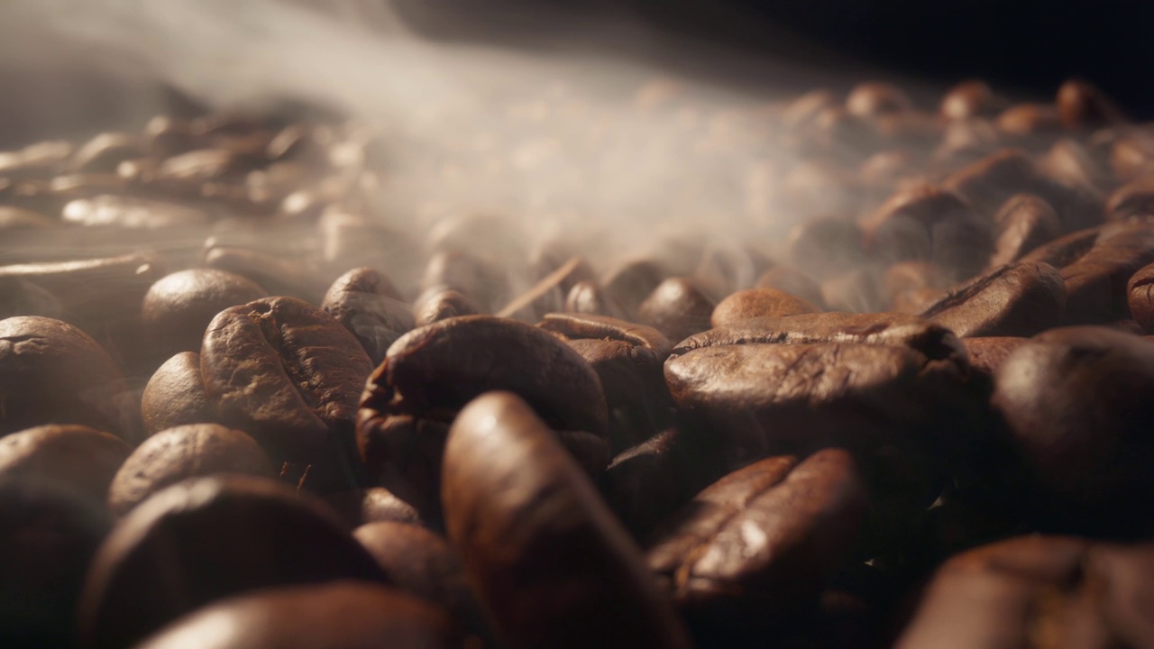 烘烤咖啡豆的过程。烟来自新鲜的咖啡籽。黑色背景下，带烟的烘焙咖啡豆滑动镜头视频素材