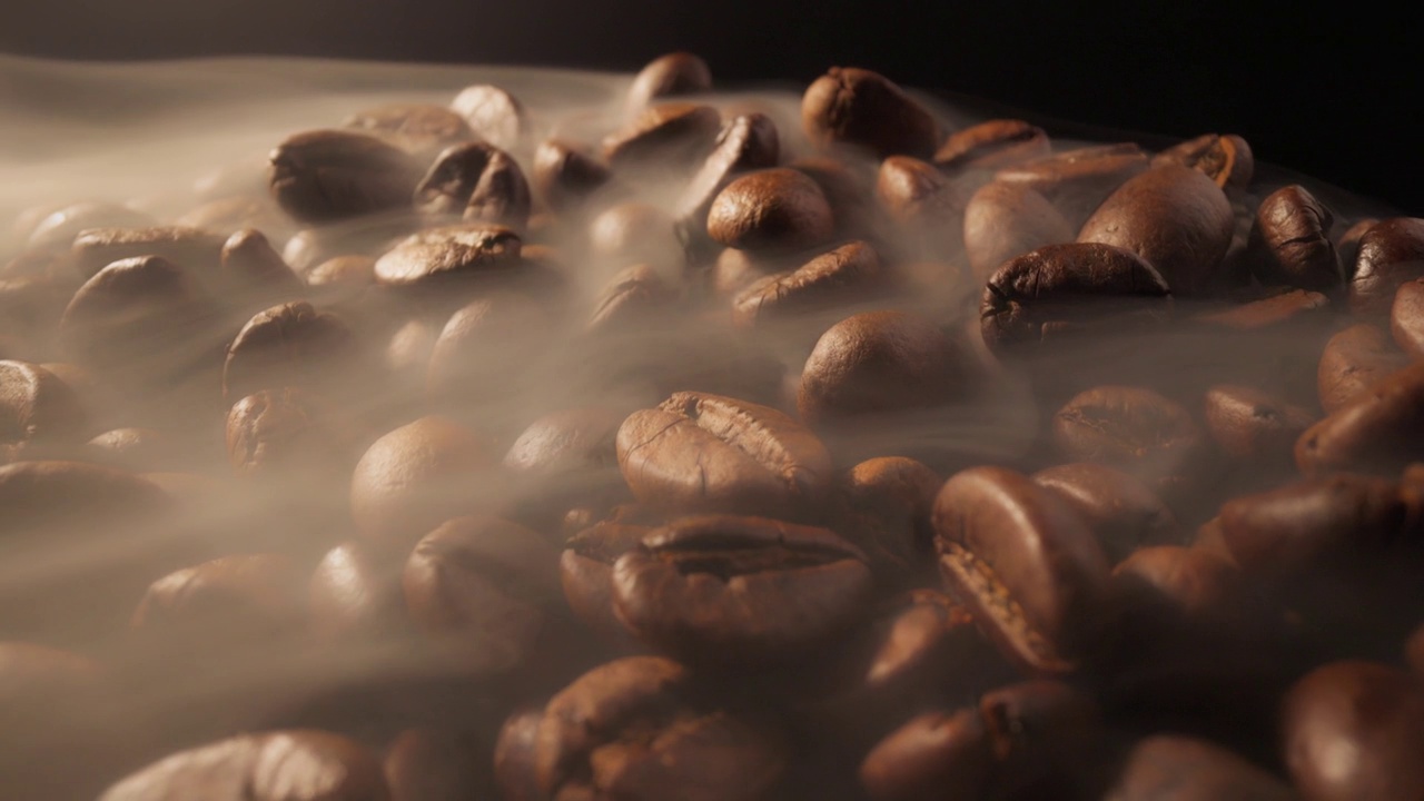 咖啡豆在烘焙过程中的滑块镜头。烟来自新鲜的咖啡籽。在黑背景下用烟熏咖啡豆视频素材