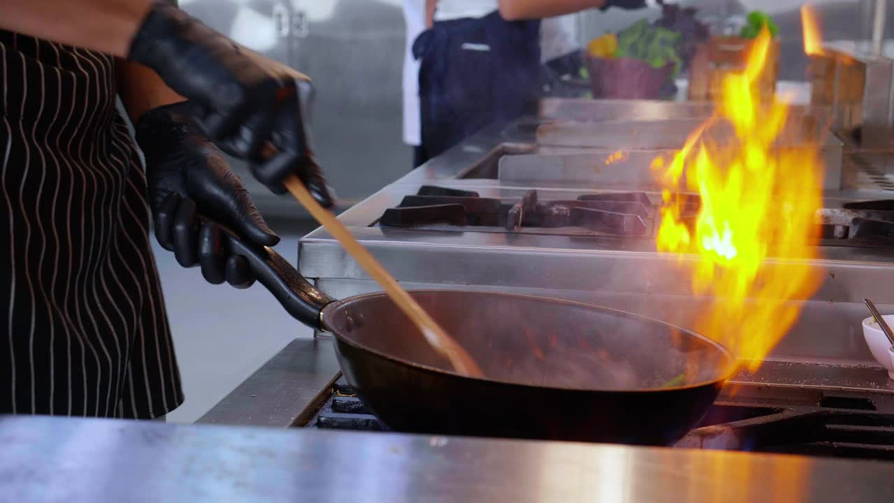 特写厨师的手炒牵牛花火焰与燃烧的锅在厨房餐厅，食物和营养，烹饪与运动慢动作，烹饪和配方。视频下载