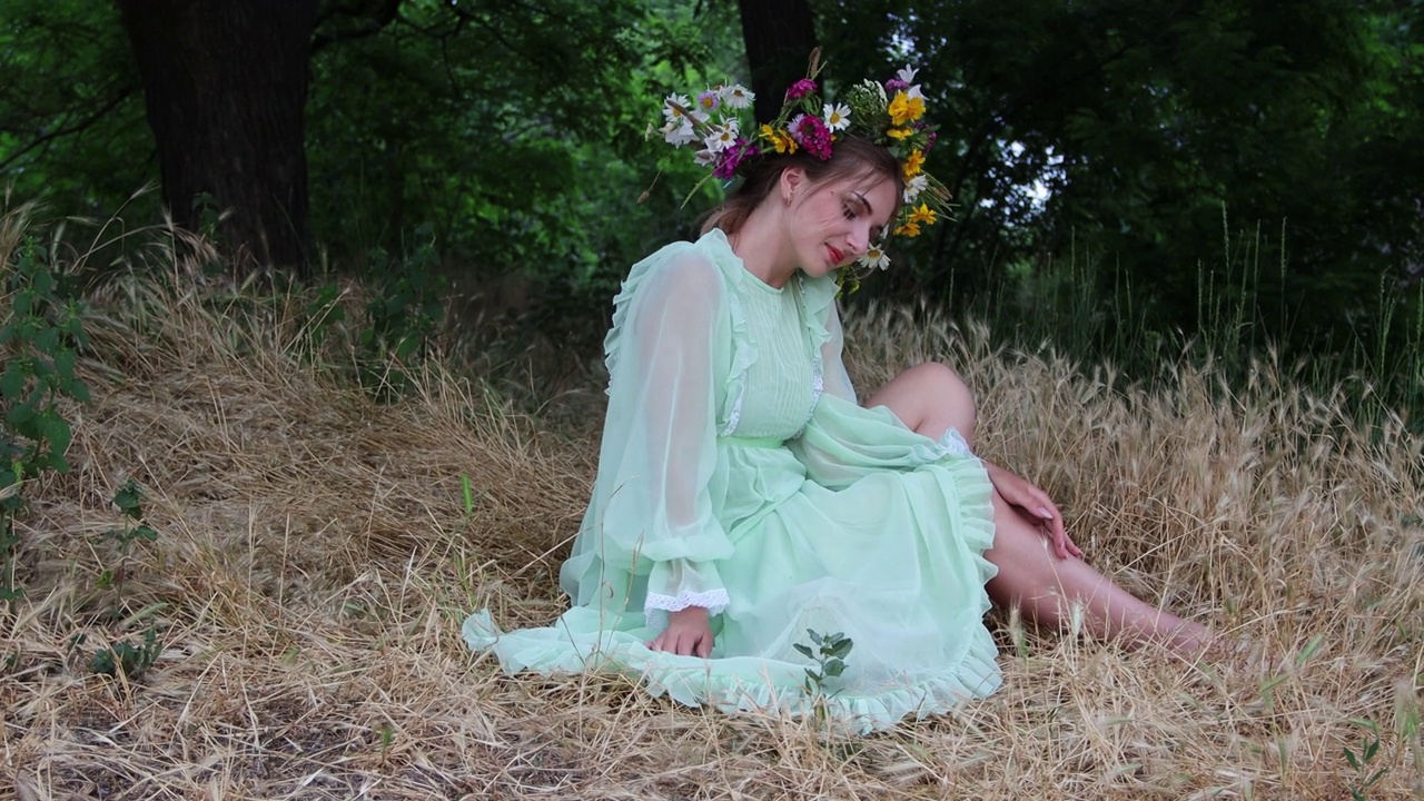 童话般的性格。美丽的女孩戴着野花花冠，穿着绿色的衣服，坐在树林里。异教信仰。森林精灵，mavka，仙女。4 k的决议视频下载