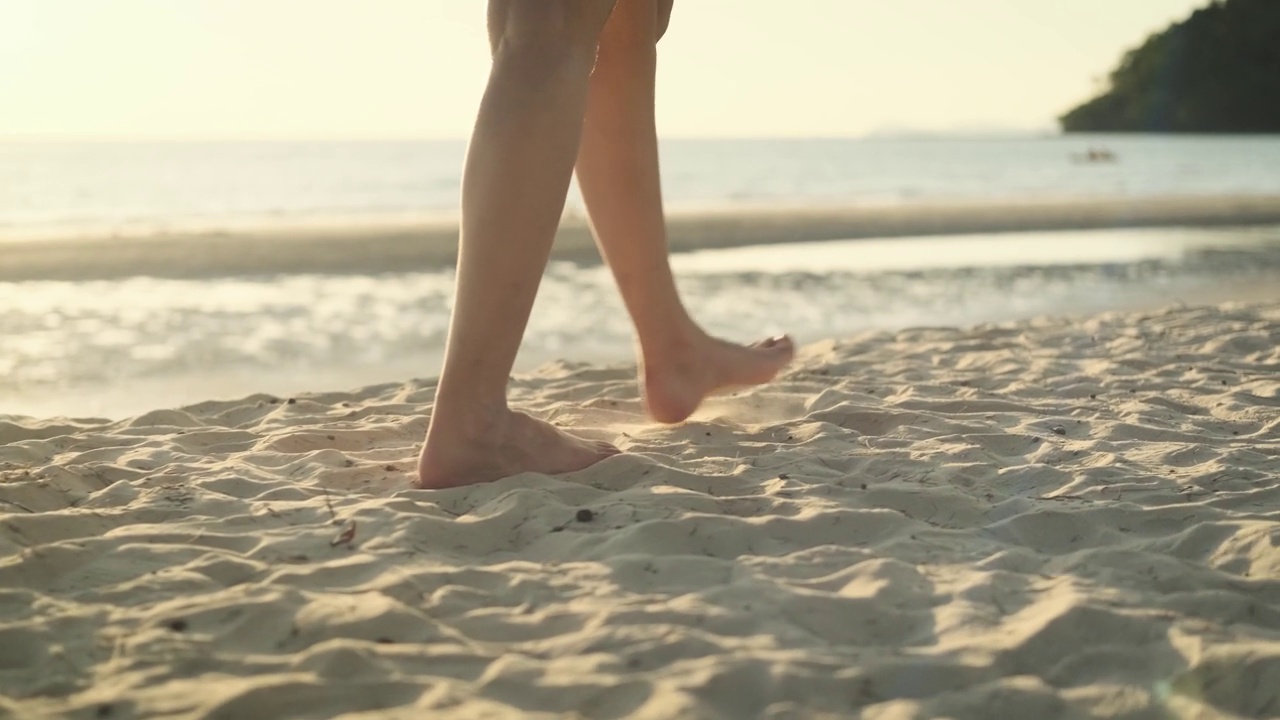 慢镜头女子赤脚走在沙滩上，在金色的日落留下脚印。在泰国度暑假的女游客。在海风吹过的洁白的沙滩上。视频下载