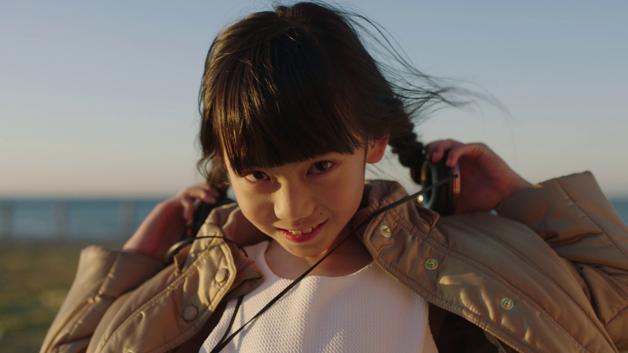 亚洲小女孩戴上耳机，在海边沙滩上听音乐，享受一天的特写视频素材