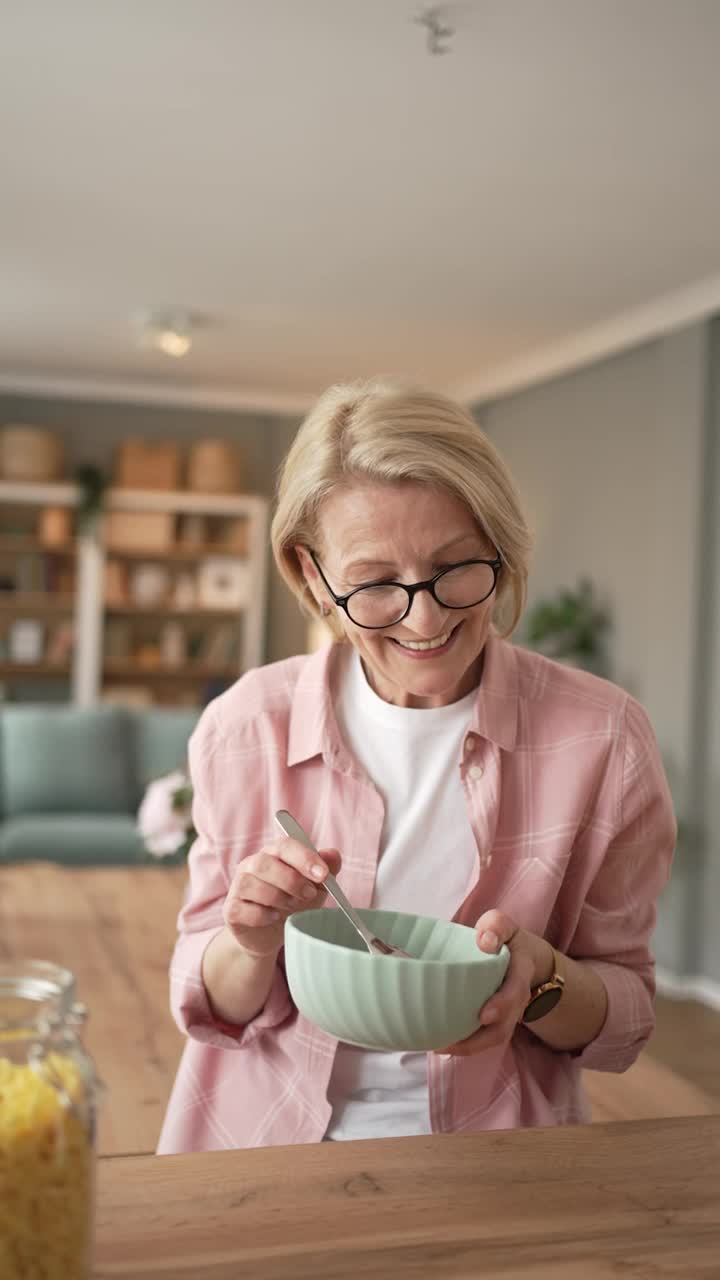 一位上了年纪的妇女像往常一样，吃着麦片和牛奶当早餐，坐在吧台的厨房里视频素材