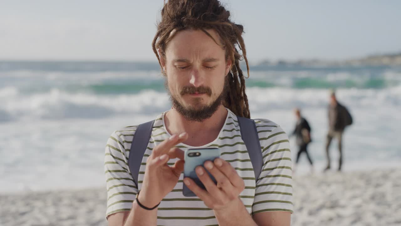 年轻的旅游男子使用智能手机短信浏览移动通信分享海滩度假冒险在线享受暑假在阳光明媚的海边视频素材