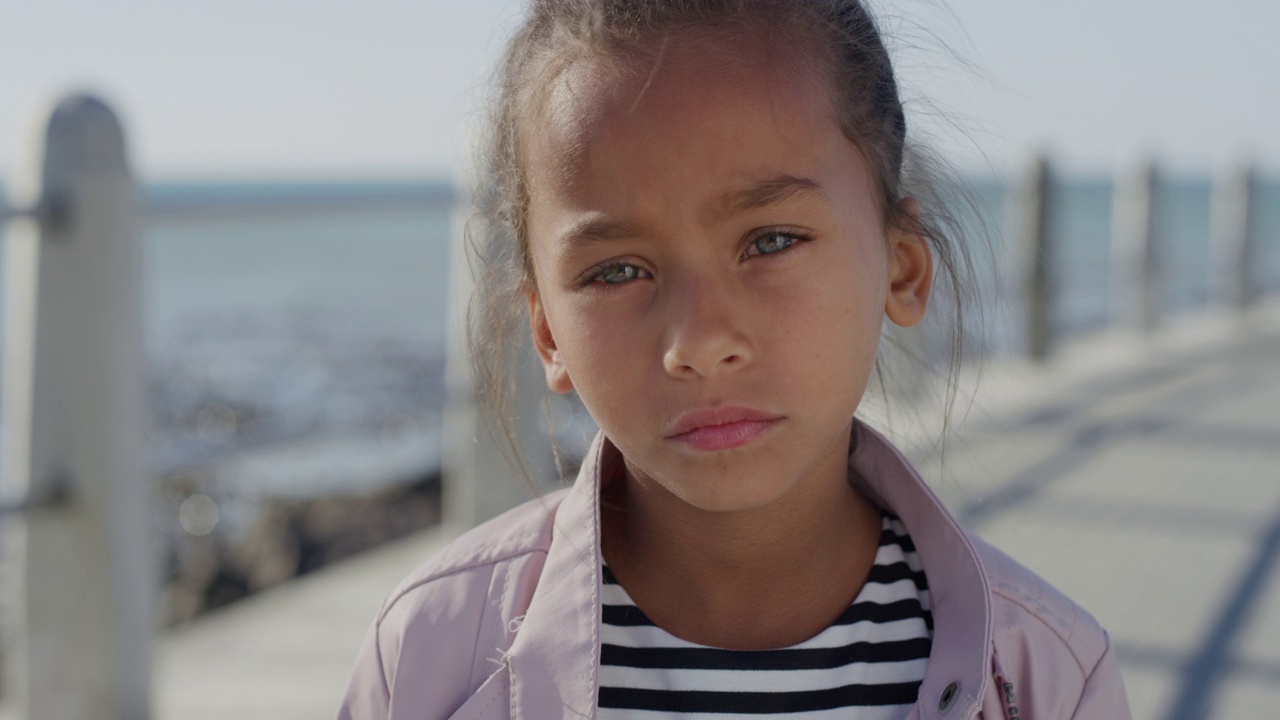 肖像年轻的小混血女孩看起来严肃沉思的孩子在阳光明媚的海边海滩真人系列视频下载
