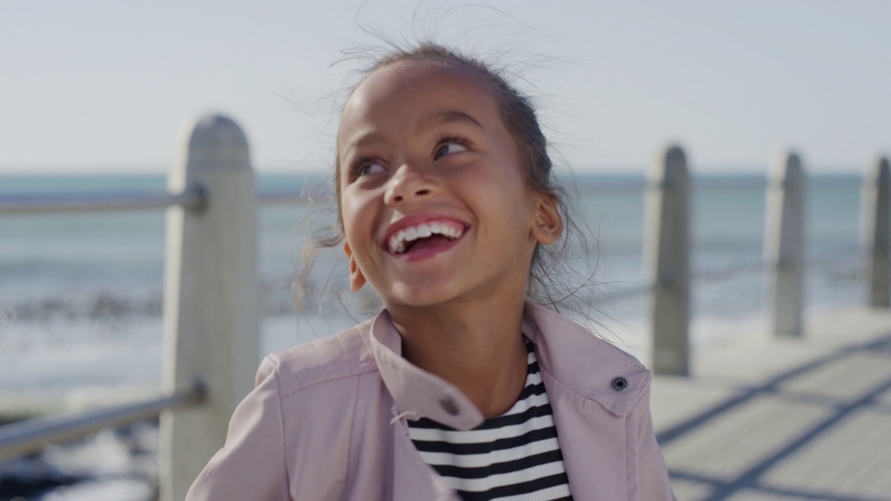 小女孩的肖像，跳舞，兴奋，笑，享受美丽的阳光明媚的一天，在海边的海滩，快乐的暑假视频素材