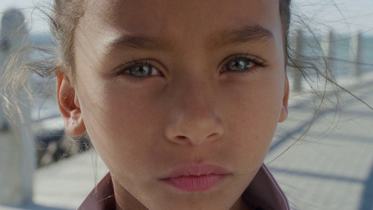 近距离肖像年轻的小混合种族女孩看起来严肃沉思的孩子在阳光明媚的海边海滩慢动作视频下载