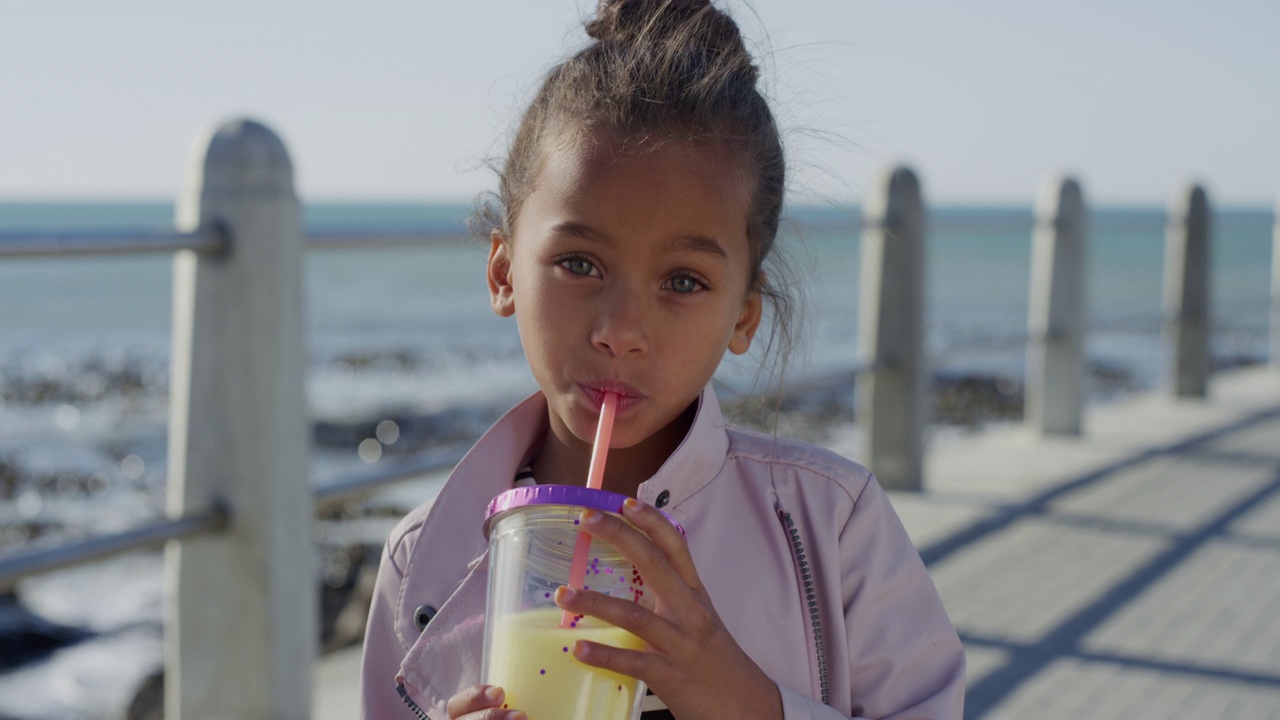 肖像美丽的小女孩喝果汁，微笑，快乐，享受温暖的暑假在海滩海滨视频素材