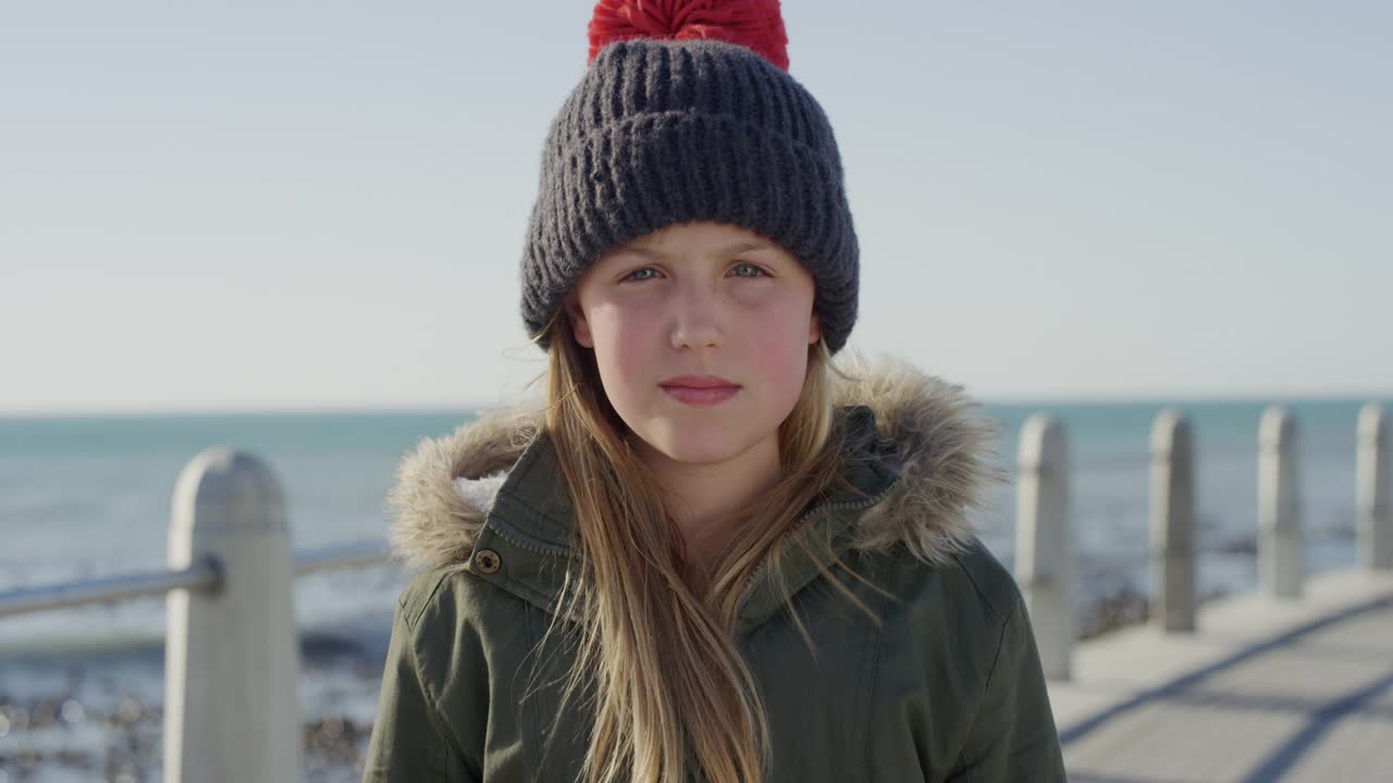 海滩上快乐的小女孩的肖像，微笑着，穿着温暖，戴着无边帽和外套视频下载