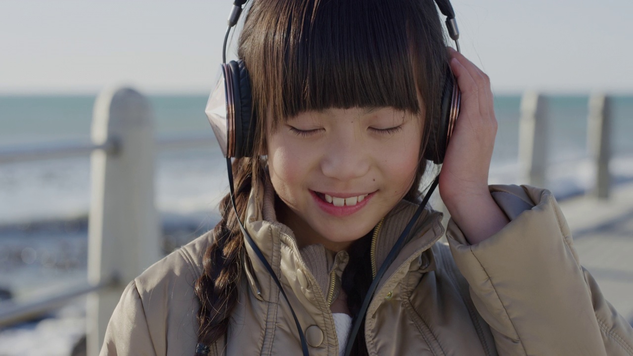 特写肖像可爱的小亚洲女孩戴着耳机微笑跳舞享受听音乐在海边的海滩视频素材