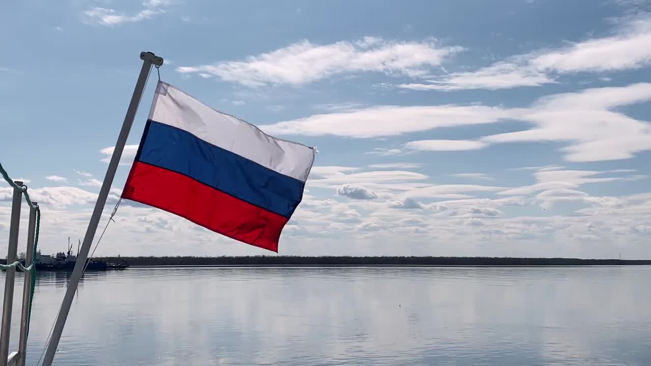 旗杆上的俄罗斯国旗在河的背景中随风飘扬。视频素材