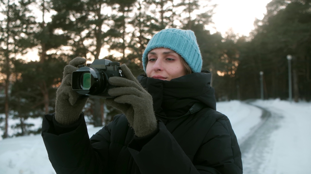 一位年轻的女摄影师在冬天的森林里用相机拍照。旅游照片视频下载