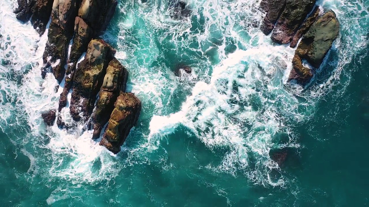 无人机拍摄的4k鸟瞰图，蓝色的海浪在岩石山的高悬崖上破碎。海滩上危险的海浪视频下载