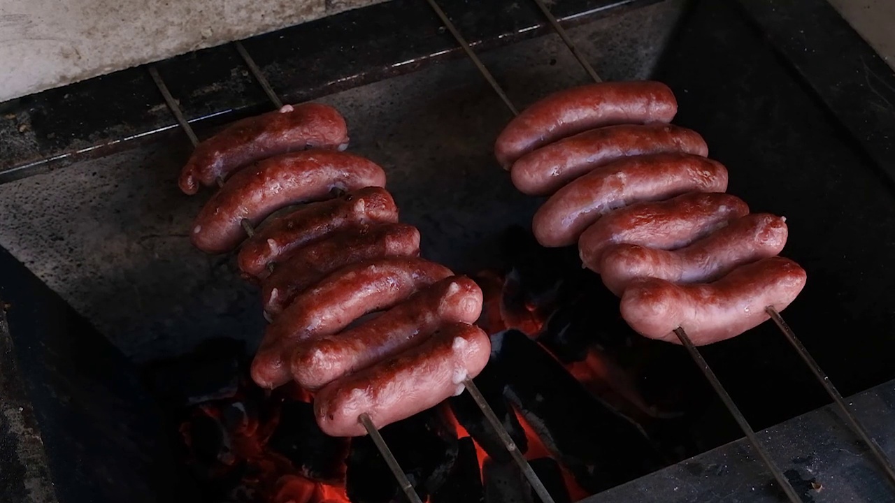 在巴西烤肉架上烤着的猪肉香肠(俯视图)。视频下载