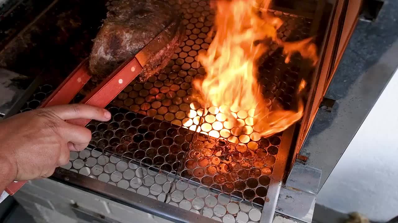 一个男人用夹子把一块驼背牛排扔进烤肉的火焰里。视频素材