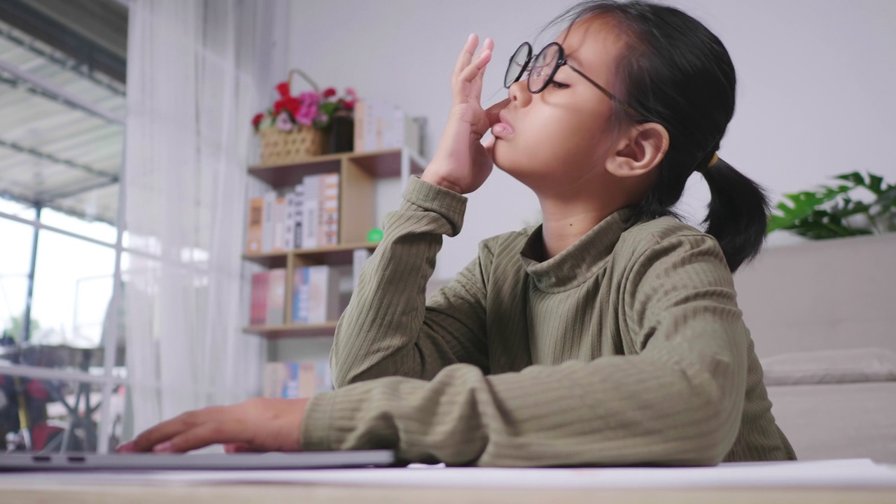 疲惫的亚洲女孩戴着眼镜，试图集中在笔记本电脑上阅读视频下载