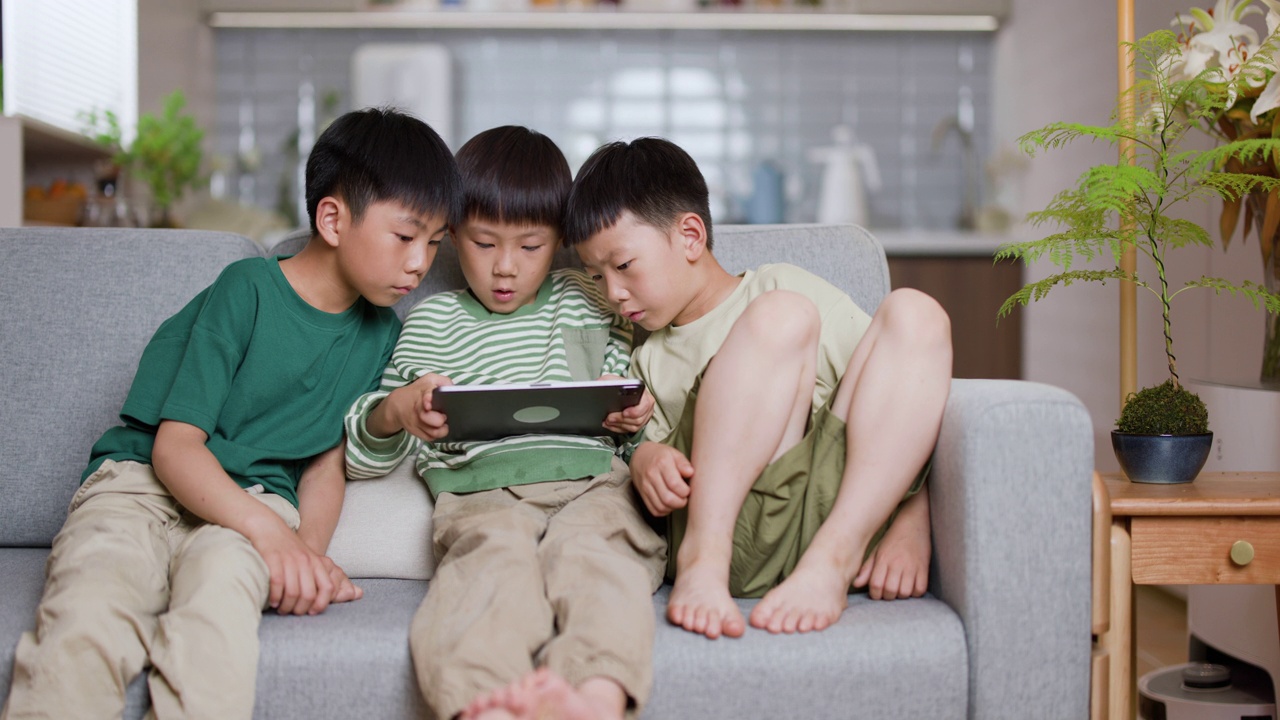 三个亚洲男孩在家里玩电子平板电脑游戏视频素材