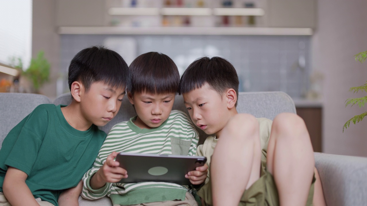 三个亚洲男孩在沙发上玩电子平板电脑视频素材