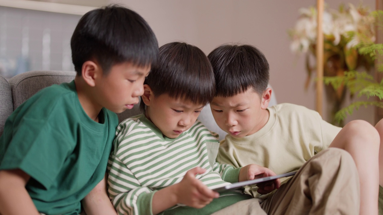 三个男孩在沙发上玩电子平板电脑视频素材