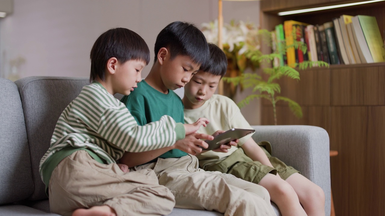 三个亚洲男孩在客厅用平板电脑玩游戏视频素材