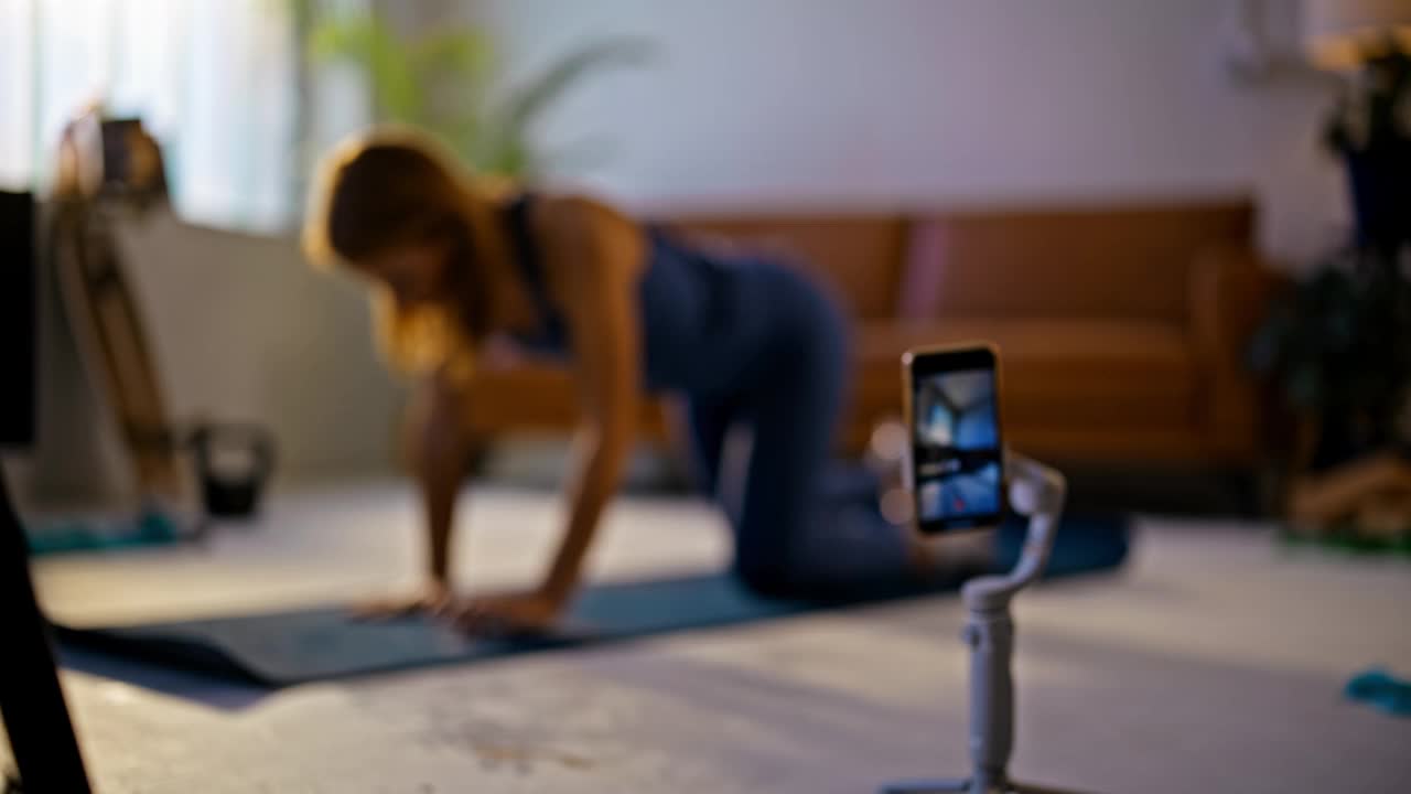 SLO MO Fit年轻的女性健身教练在客厅的瑜伽垫上交替进行手臂和腿的抬高，在智能手机屏幕后拍摄家庭锻炼。视频博客,影响健康的生活方式,锻炼。以8K分辨率拍摄。视频下载