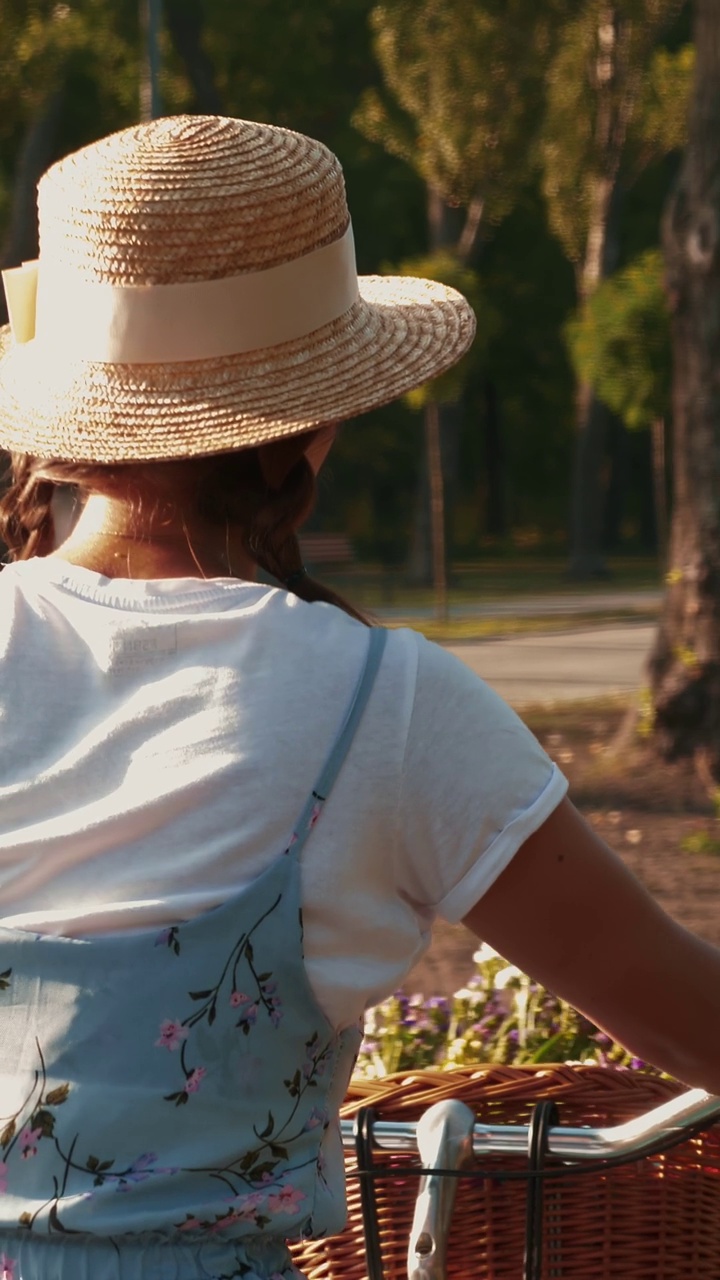 夏天，戴草帽的女子在公园里骑着复古自行车。垂直视频视频下载