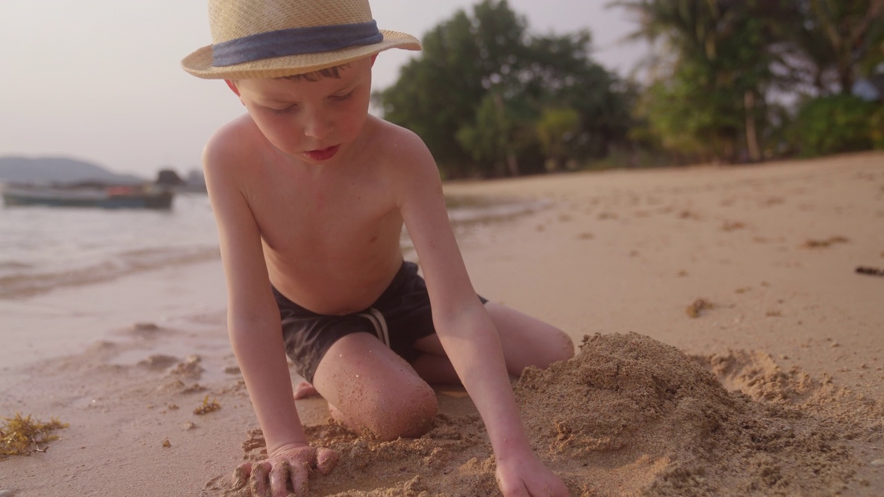 男孩在泰国海滩上挖沙子视频素材