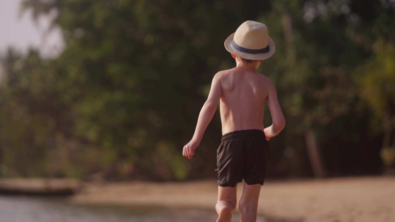 戴着帽子的男孩在沙滩上奔跑视频素材