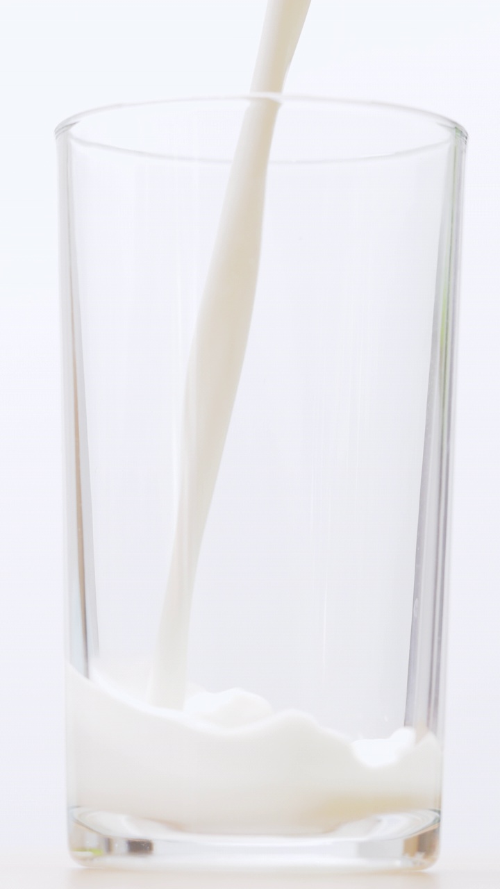 将鲜牛奶倒入白色背景的透明玻璃杯中。视频素材