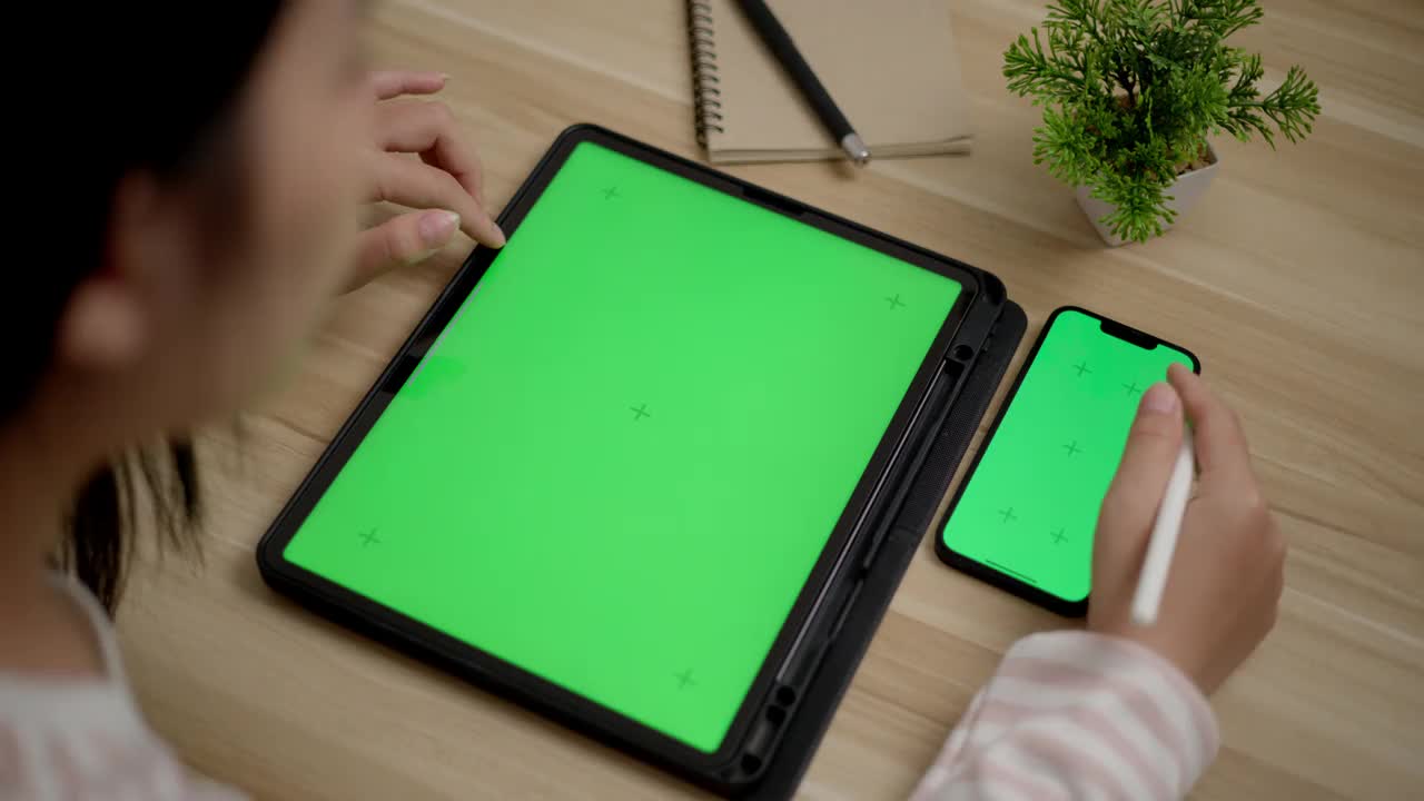 年轻女性在智能手机和平板电脑上工作，模拟绿色屏幕空白视频素材