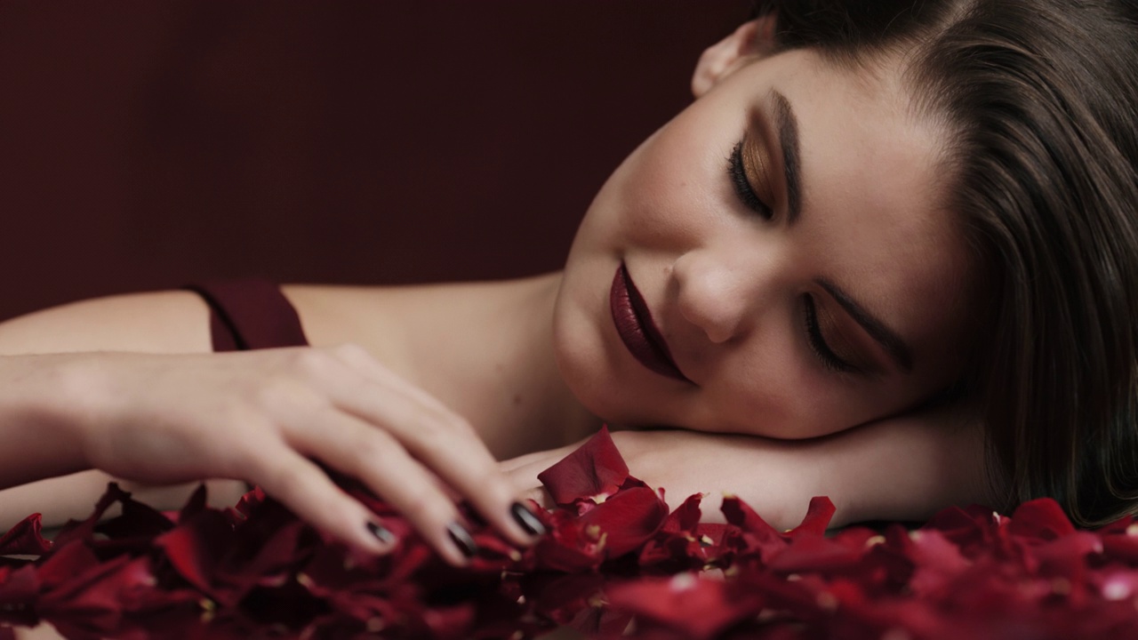肖像美丽的高加索妇女玩玫瑰花瓣下降感性的女性梦想亲密的幻想浪漫放纵欲望在红色背景情人节的概念视频下载