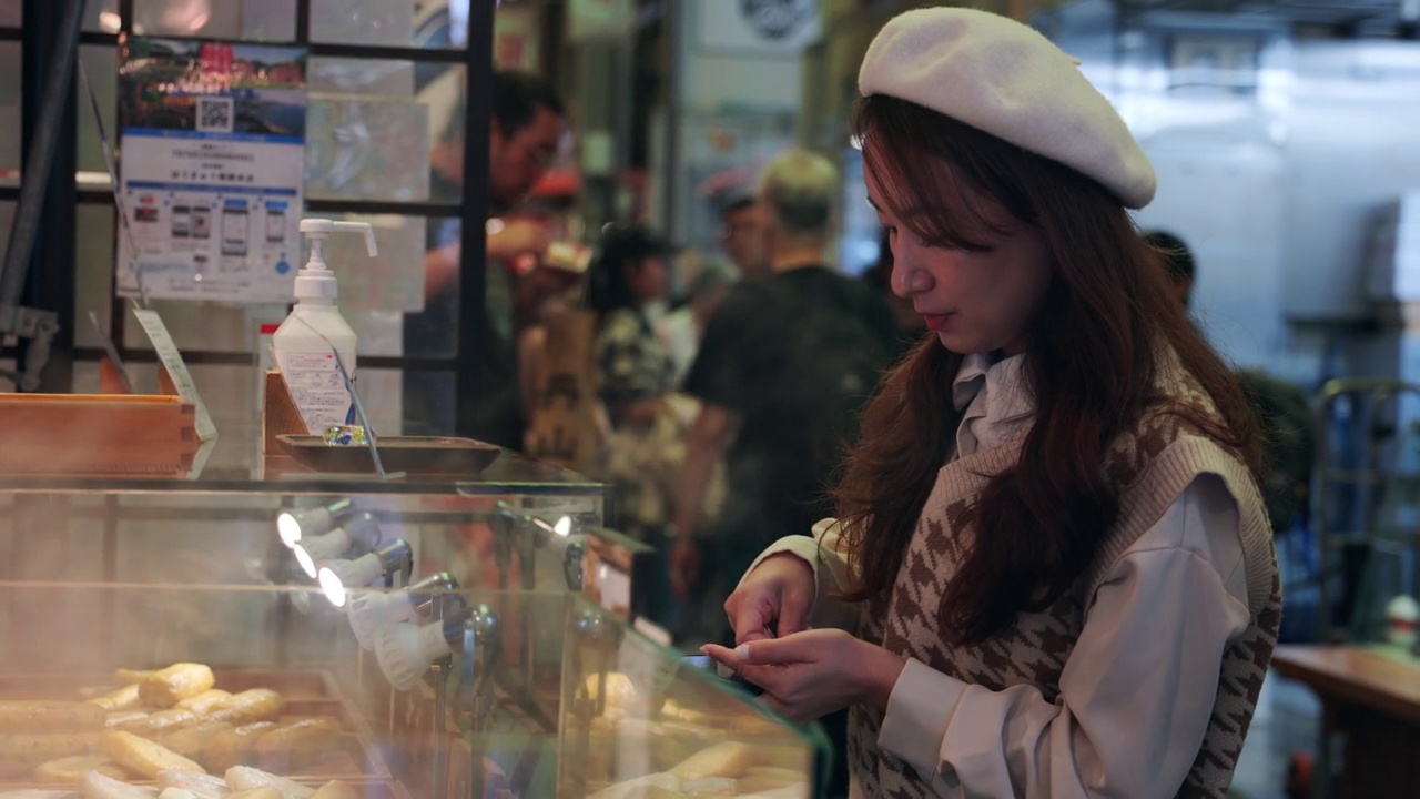 一位亚洲妇女在日本京都的西木市场观光。她走近当地的食品摊贩，下订单，购买食品。视频下载