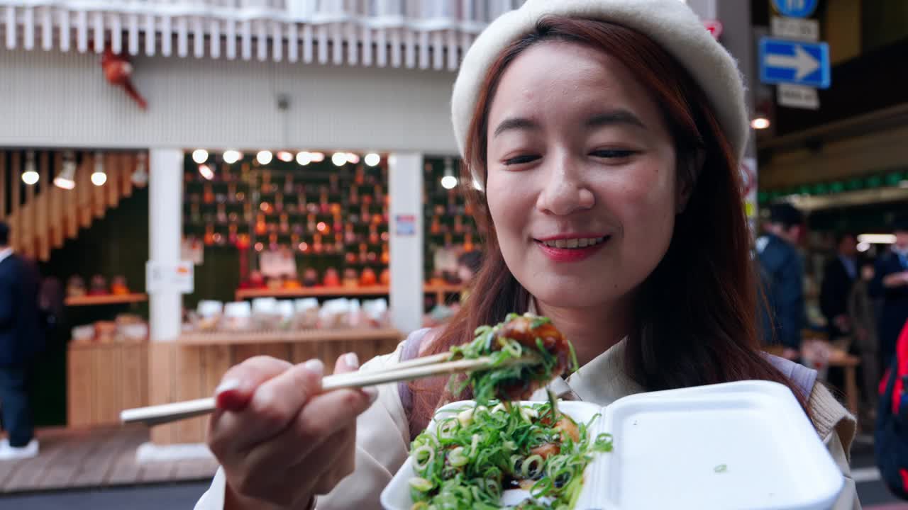 一位亚洲妇女正在品尝日本料理，这是在京都西木市场发现的一种受欢迎的美食。她沉浸在当地的饮食和文化中。视频下载