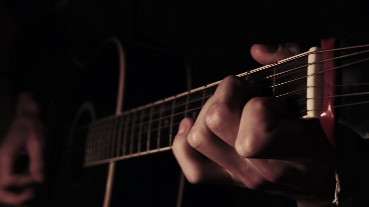 男子在家中在大气黑暗温暖的灯光下弹奏原声吉他视频下载