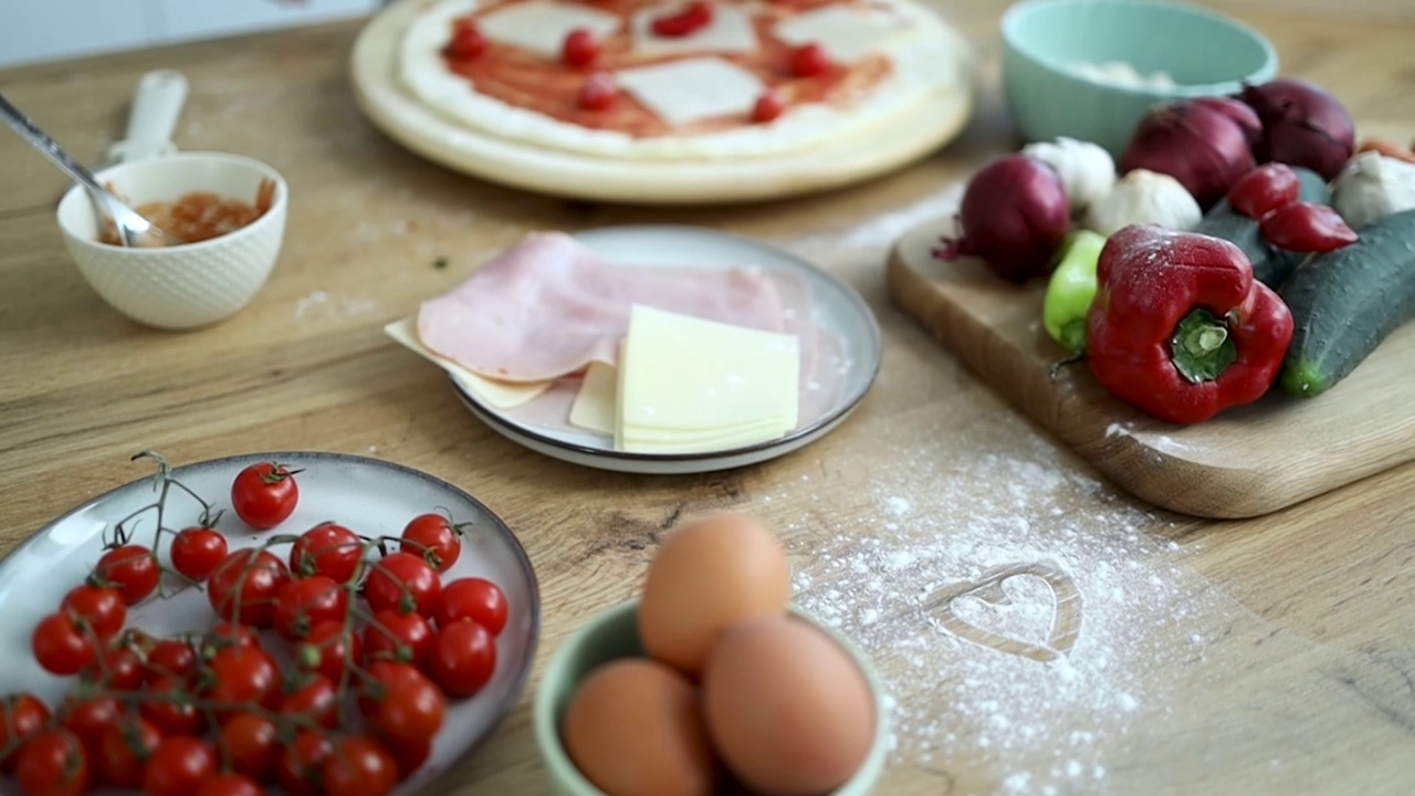 擀好的披萨面团放在桌子上，用面粉、西红柿、鸡蛋、木制的传统盘子、器具。自制烘焙食品视频下载