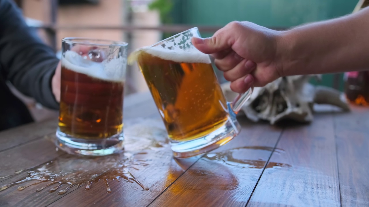两只手碰碰啤酒杯的特写镜头，撞击时泡沫溢出。视频下载