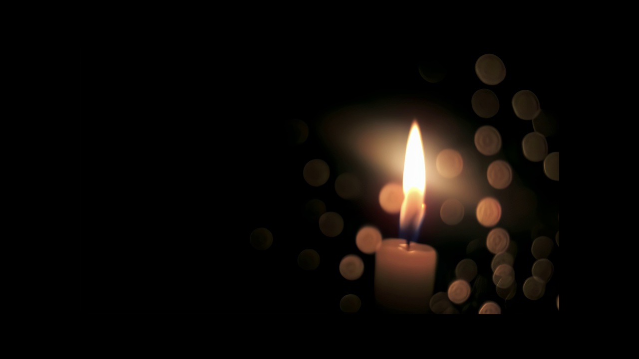 特写，燃烧的蜡烛芯后面的玻璃与散景滴，在黑色的背景覆盖。视频下载