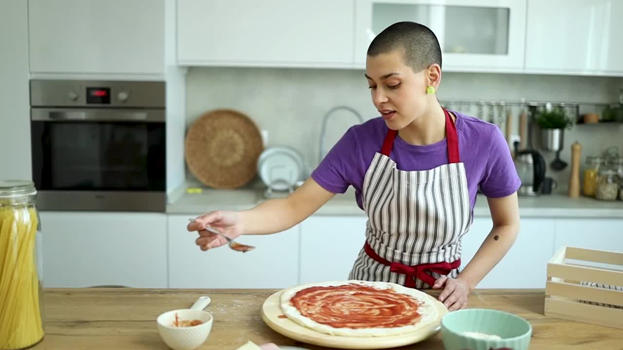 一个短发的年轻女孩在一个现代化的厨房里做披萨视频下载
