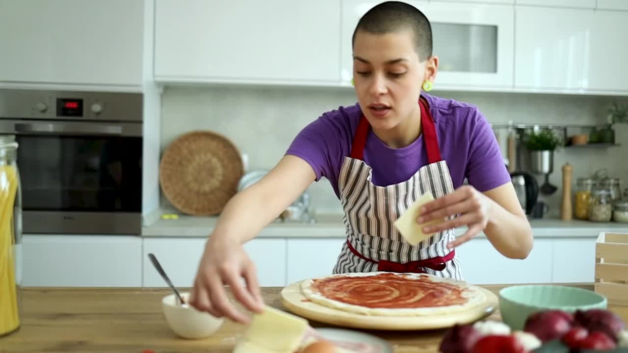 一个短发的年轻女孩在一个现代化的厨房里做披萨视频下载
