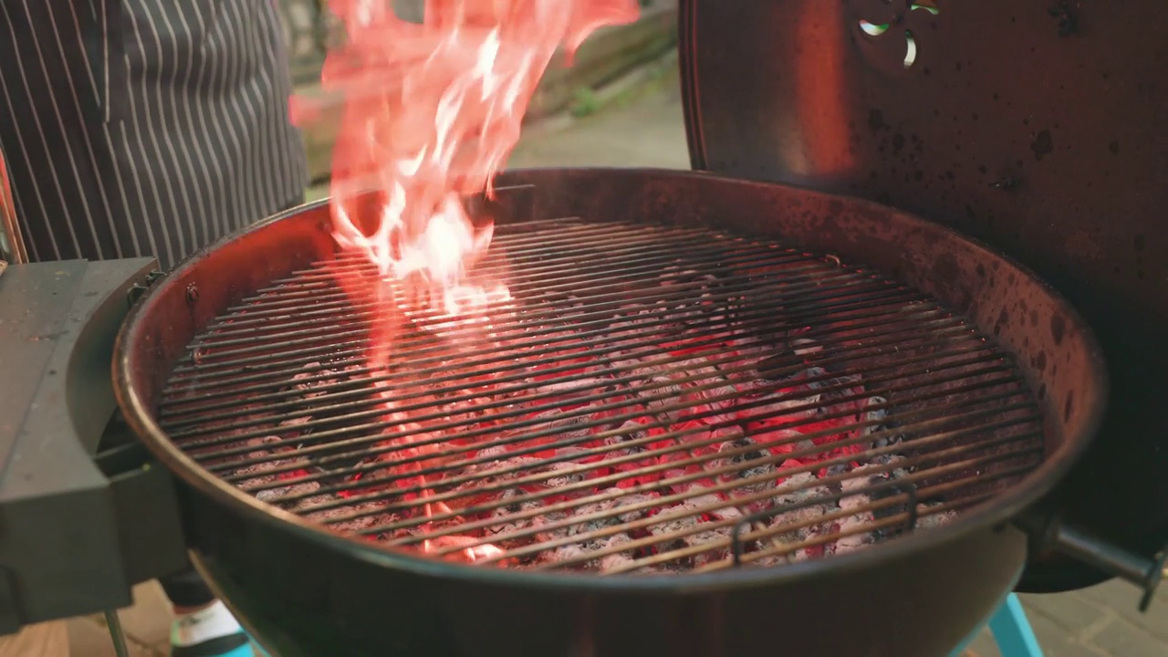 金属火盆的特写。一个拿着烧烤钳的男人的手在烤架上抹油，以便煎肉。烹调:烹调肉的过程这个人正在烤烤架。视频下载
