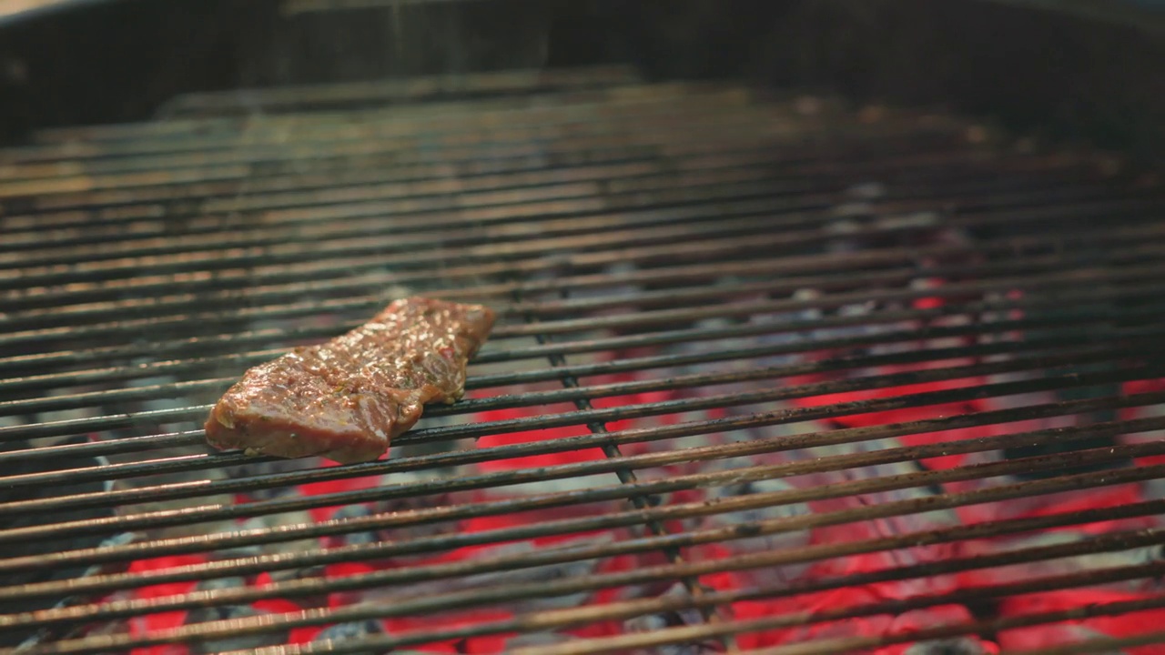 一个男人的手把多汁的肉块放在金属格栅上烧烤，在露天的篝火上烹饪。夏日家庭野餐，户外美食。视频下载