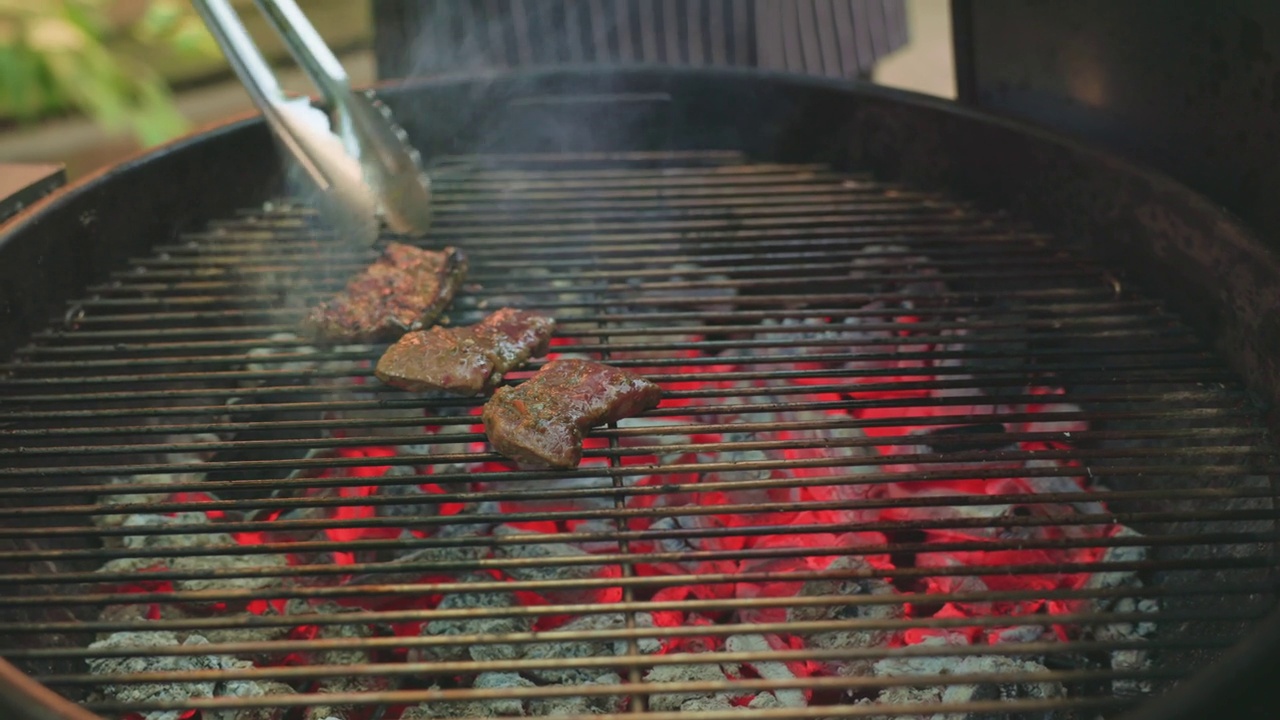 烧烤架外烤牛肉肉用热铁烤制。厨师用火钳把烤肉排上的肉片转到火上，产生火花，制作出美味的街头小吃。视频下载