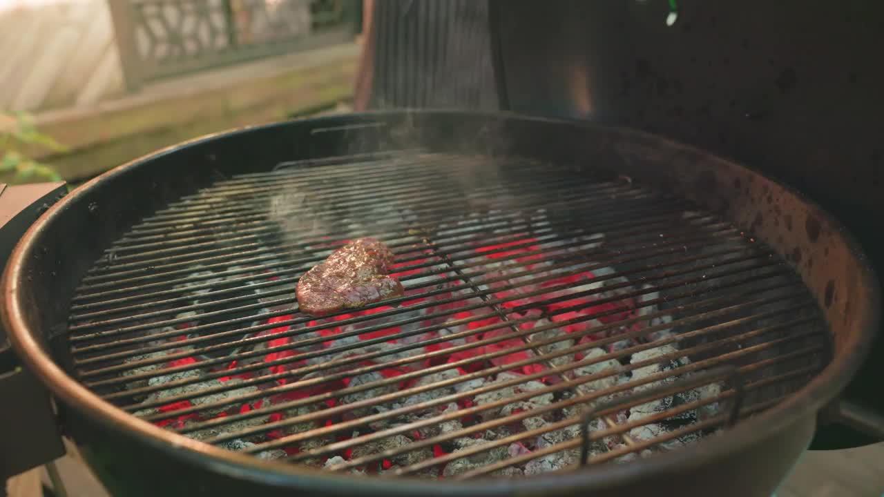 一个男人的手把多汁的肉块放在金属格栅上烧烤，在露天的篝火上烹饪。夏日家庭野餐，户外美食。视频下载