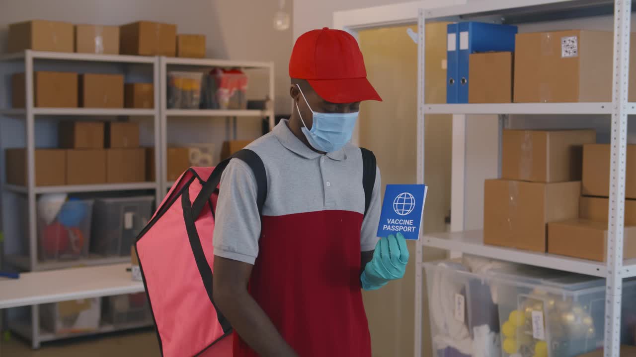 非洲快递员的肖像，戴着安全口罩和手套，拿着免疫护照看着相机视频下载