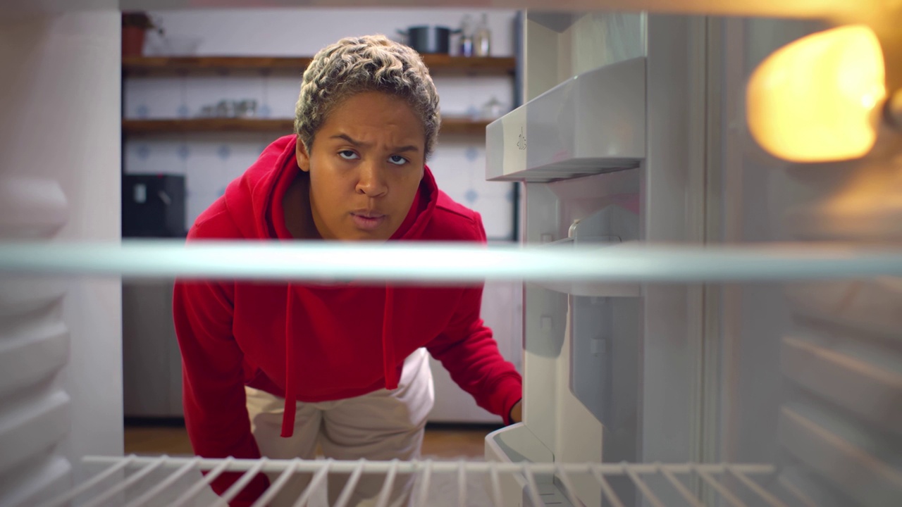 一位年轻的非裔美国妇女看着空空的冰箱。实时视频下载