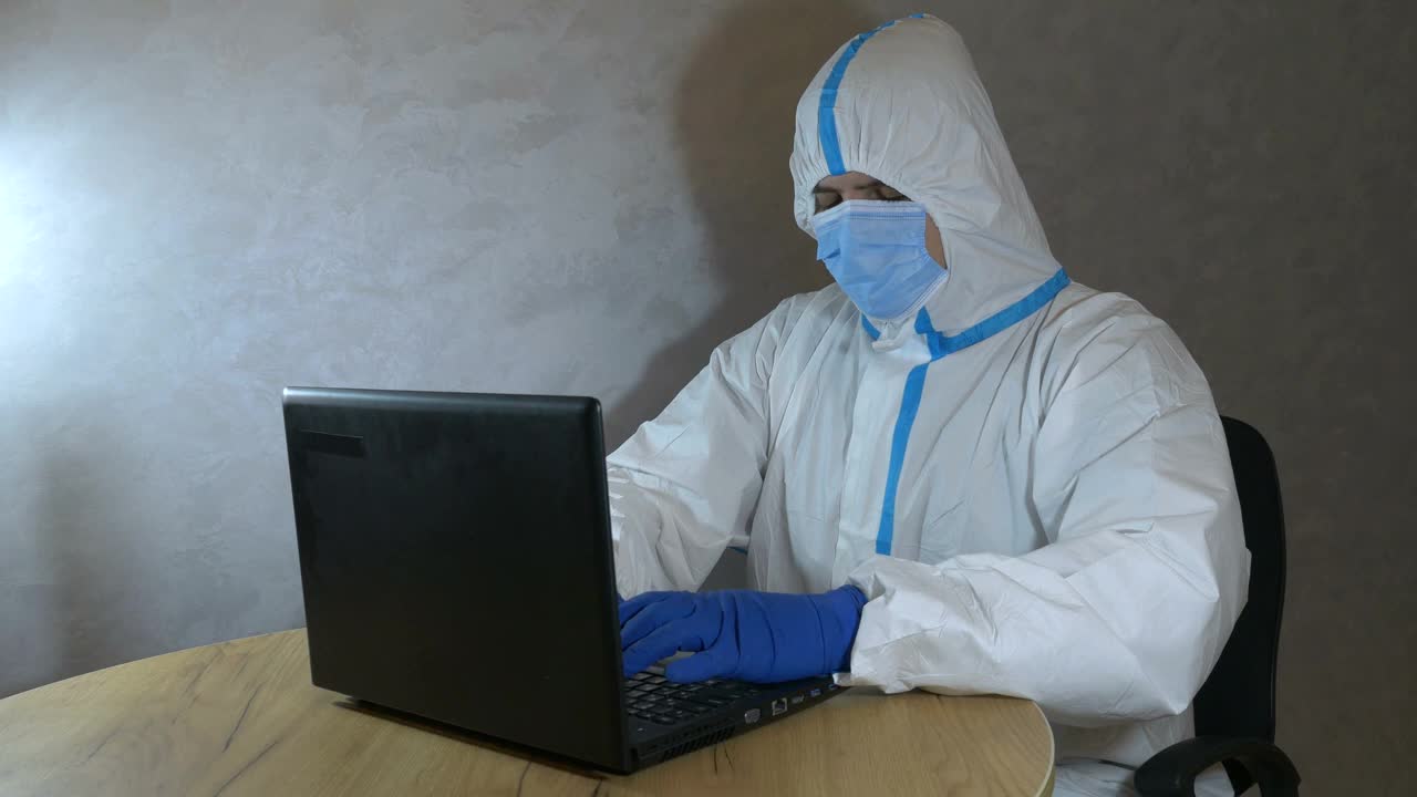 医生穿着医疗防护服，戴着医用口罩和手套，在笔记本电脑上工作。病毒流行保护mers。冠状病毒(COVID-19)。医疗保健的概念。大流行疫情下的远程工作。视频下载